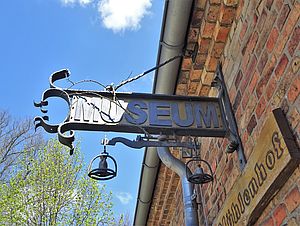Der Blick geht auf ein schmiedeeisernes Schild "Museum" an einer Ziegelwand.