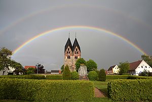 Blick über den Dorfanger Lugau bis zur Kirche. Diese wird von einem Regenbogen eingerahmt.
