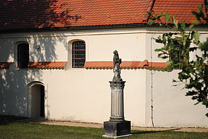 Blick auf einen Teil der Dobraer Kirche. Im Vordergrund steht eine Steinsäule mit einer Frauengestalt