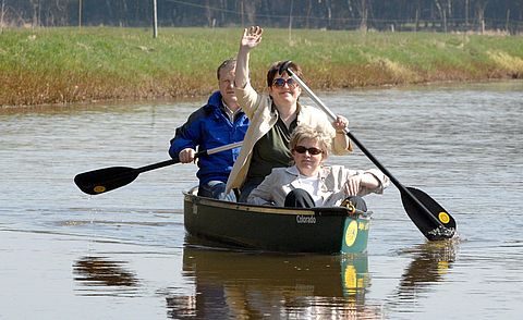 Drei Personen sitzen in einem Boot. Zwei halten ein Paddel