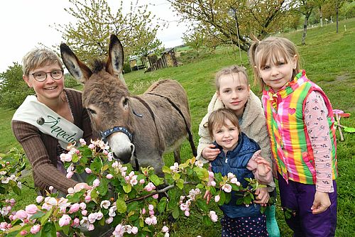 Äppelmoid Jana Reichel mit Esel und drei Kindern hinter blühendem Obststrauch