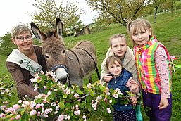Äppelmoid Jana Reichel mit Esel und drei Kindern hinter blühendem Obststrauch